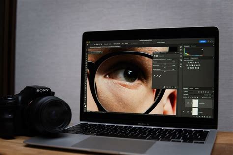 Photographer using a laptop with Photoshop open, displaying a portrait with a digital background.