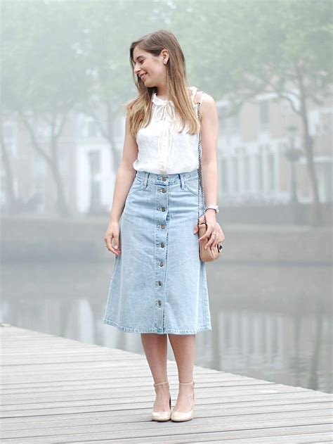 A person wearing a white t-shirt, a denim jacket, and a midi ruffle skirt in a park.